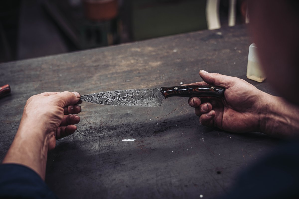 Haende pruefen die Geometrie einer handgeschmiedeten Damastklinge