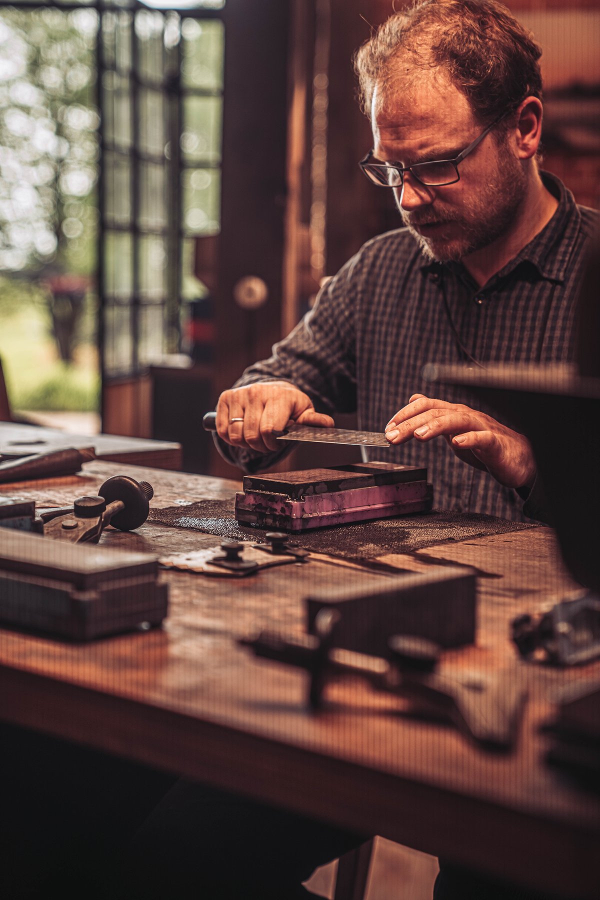 Messerschmied schaerft eine Damastklinge von Hand auf einem japanischen Schleifstein