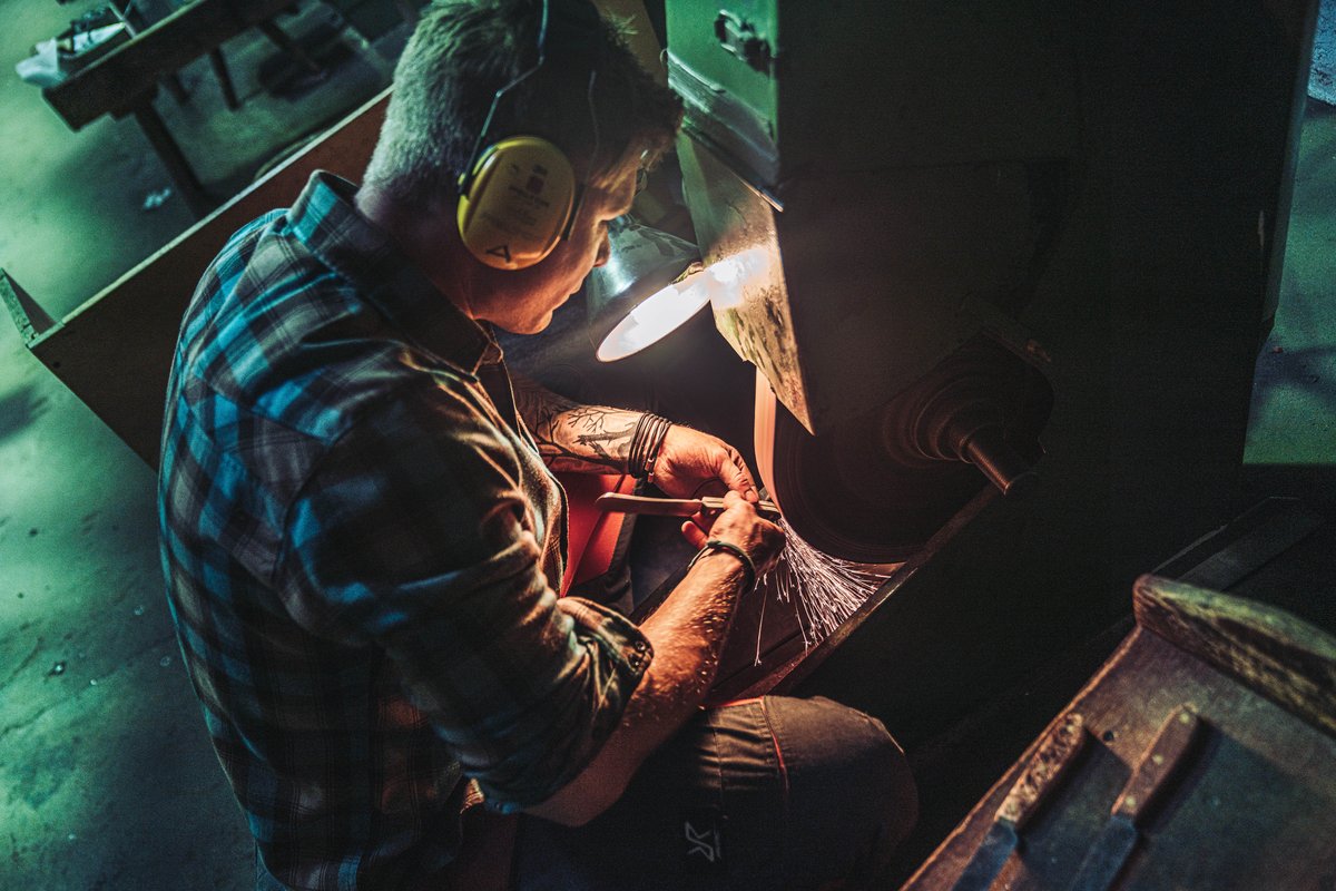 Handwerker schleift eine Messerklinge am Bandschleifer bei Otter-Messer mit Funkenflug