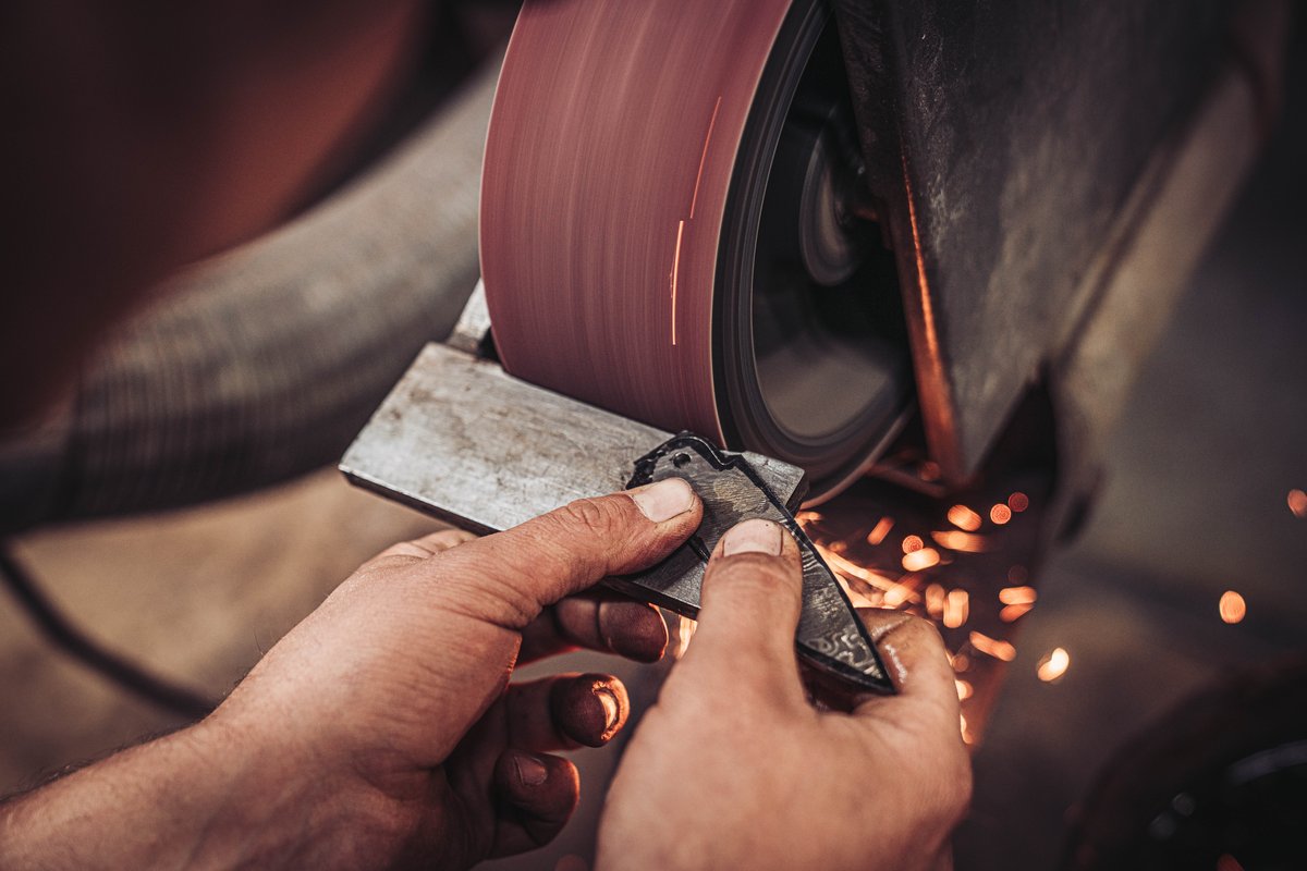 Kunstvoller Feinschliff eines Damaststahl-Werkst&uuml;cks am Bandschleifer mit Funkenflug