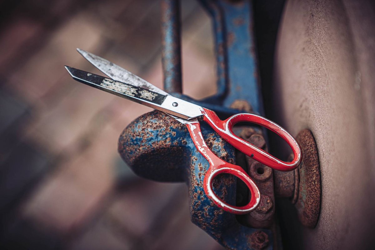 Abgenutzte rote Haushaltsschere mit Gebrauchsspuren auf einem alten Schraubstock