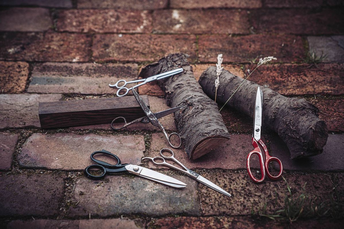 Fuenf verschiedene Scherentypen auf Backsteinpflaster von Stoffschere bis Friseurschere