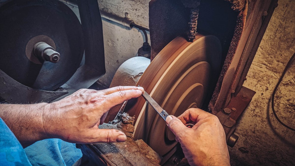 Ein einzelnes Scherenblatt wird am Schleifstein geschaerft