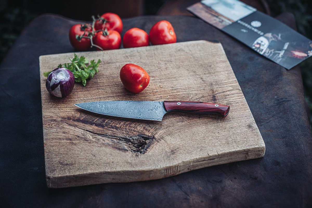Handgeschmiedetes Damastmesser mit Tomaten auf rustikalem Holzbrett f&uuml;r den Tomatentest