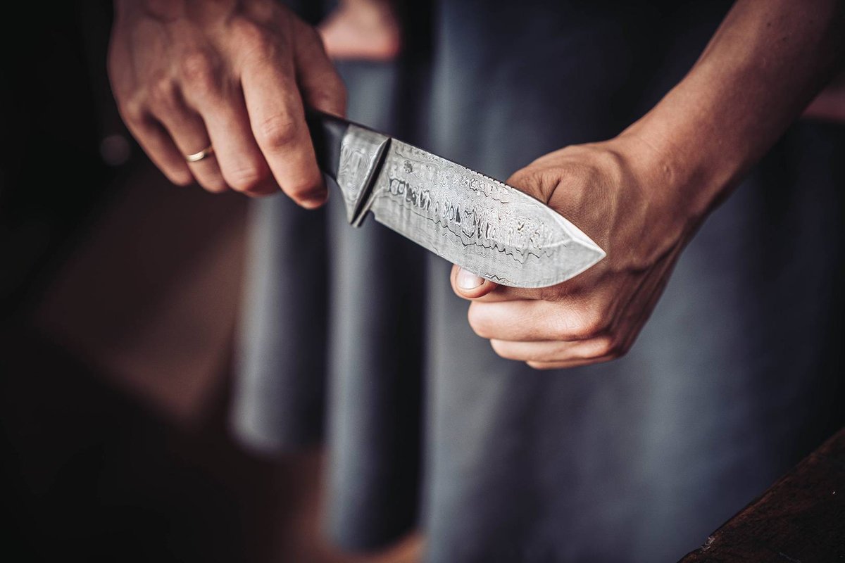 H&auml;nde pr&uuml;fen die Schneide einer handgeschmiedeten Damastklinge