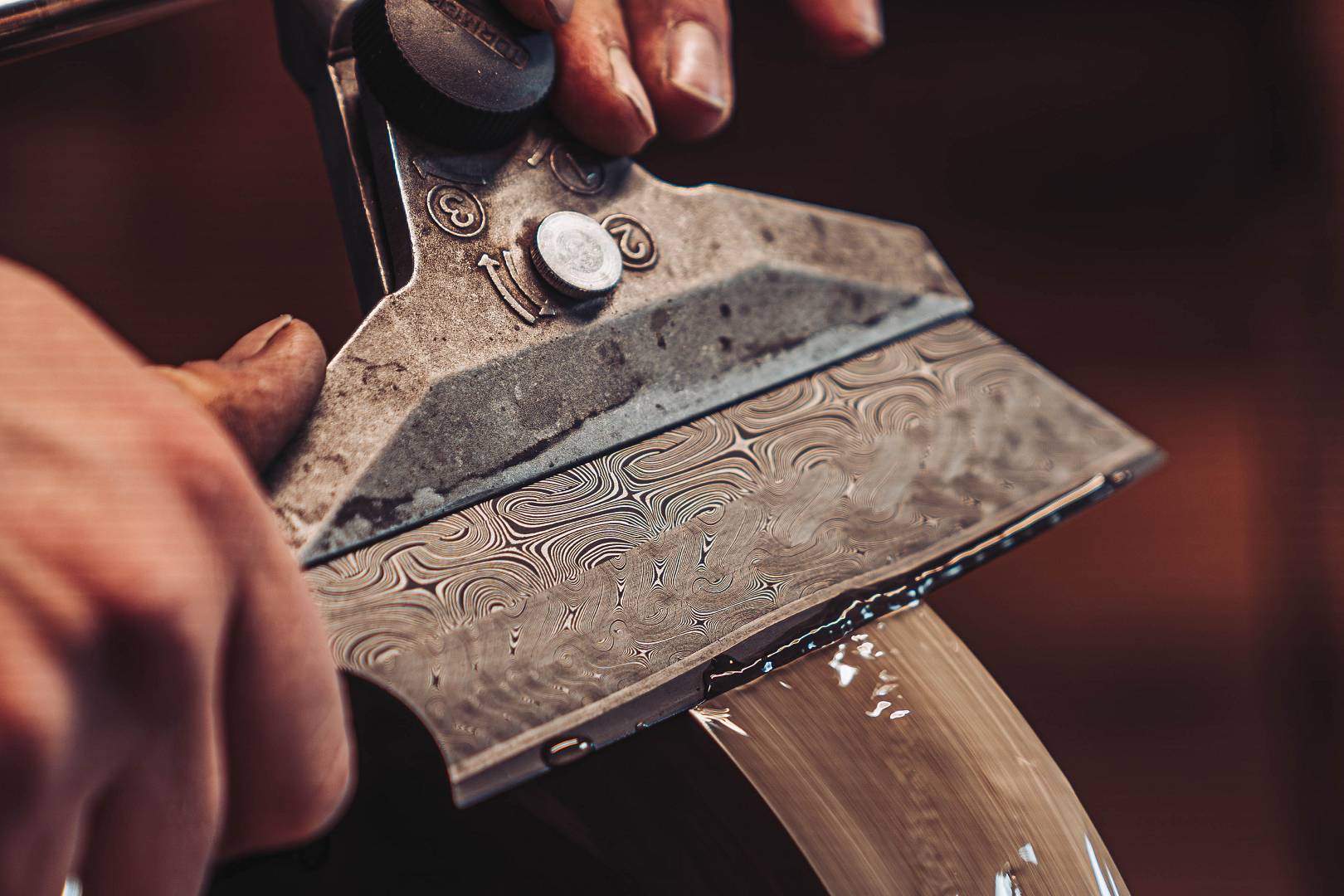 Damastklinge wird unter Wasserkuehlung am Nassschleifer geschaerft