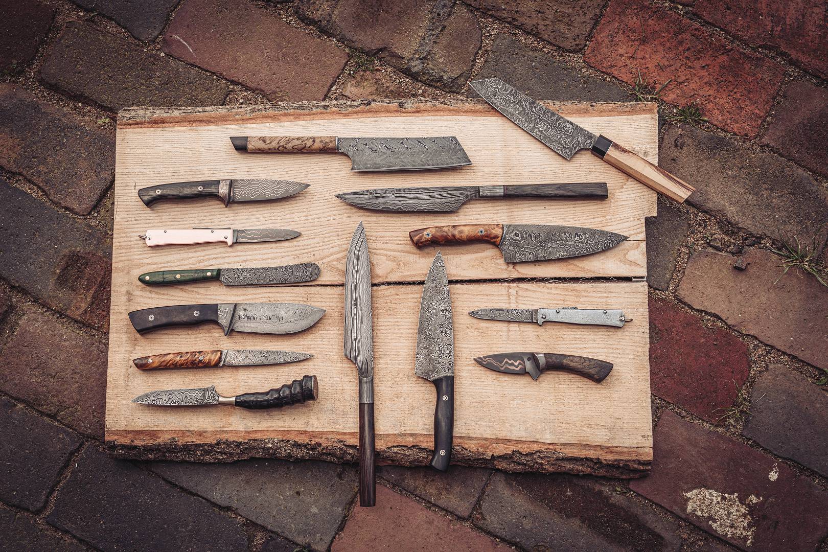 Sammlung verschiedener Damastmesser auf Holzbrett — Kuechen-, Jagd- und Klappmesser