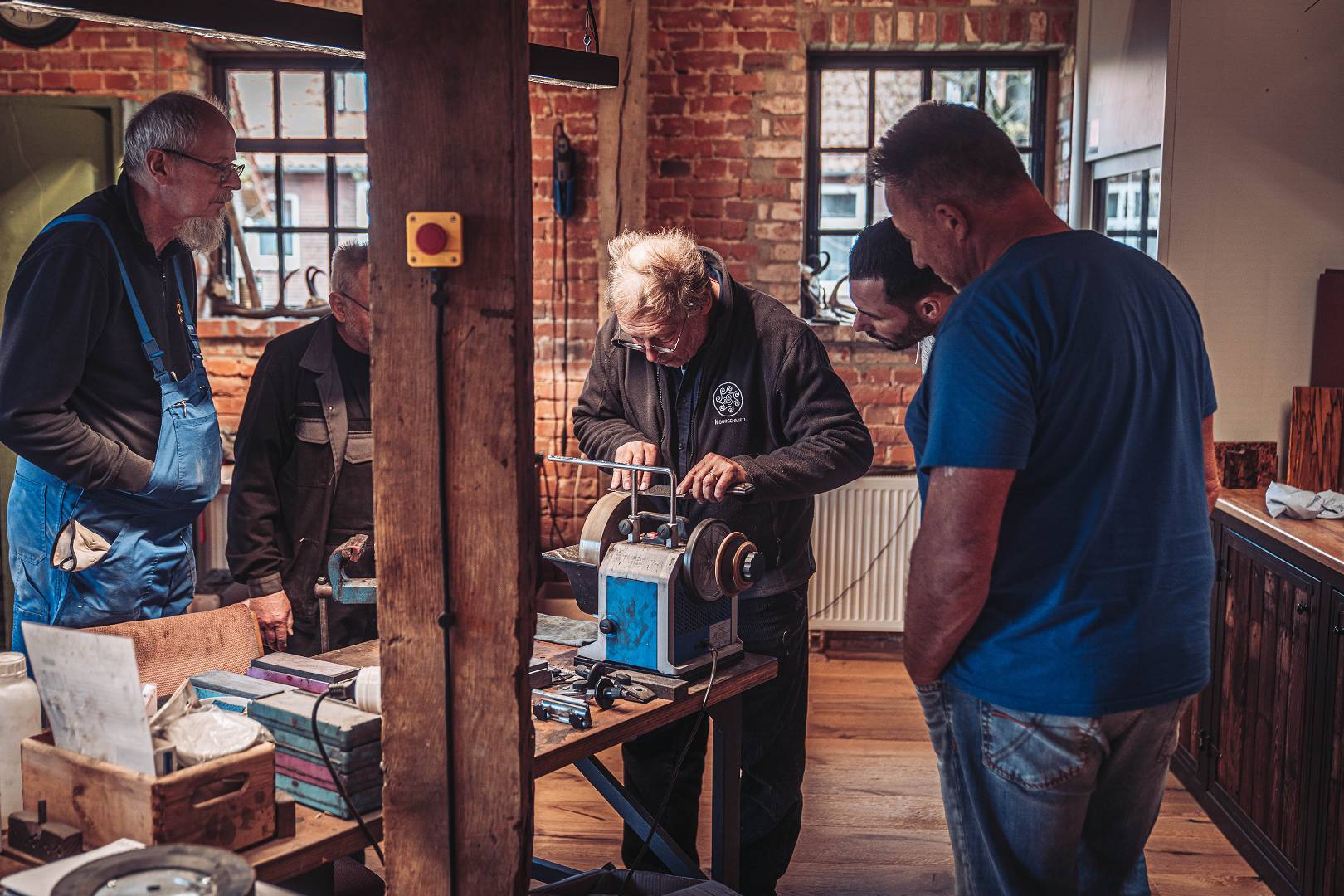 Kursleiter demonstriert an der Werkbank vor Kursteilnehmern in der Alten Schmiede &mdash; Backsteinw&auml;nde, Werkzeuge, konzentrierte Blicke