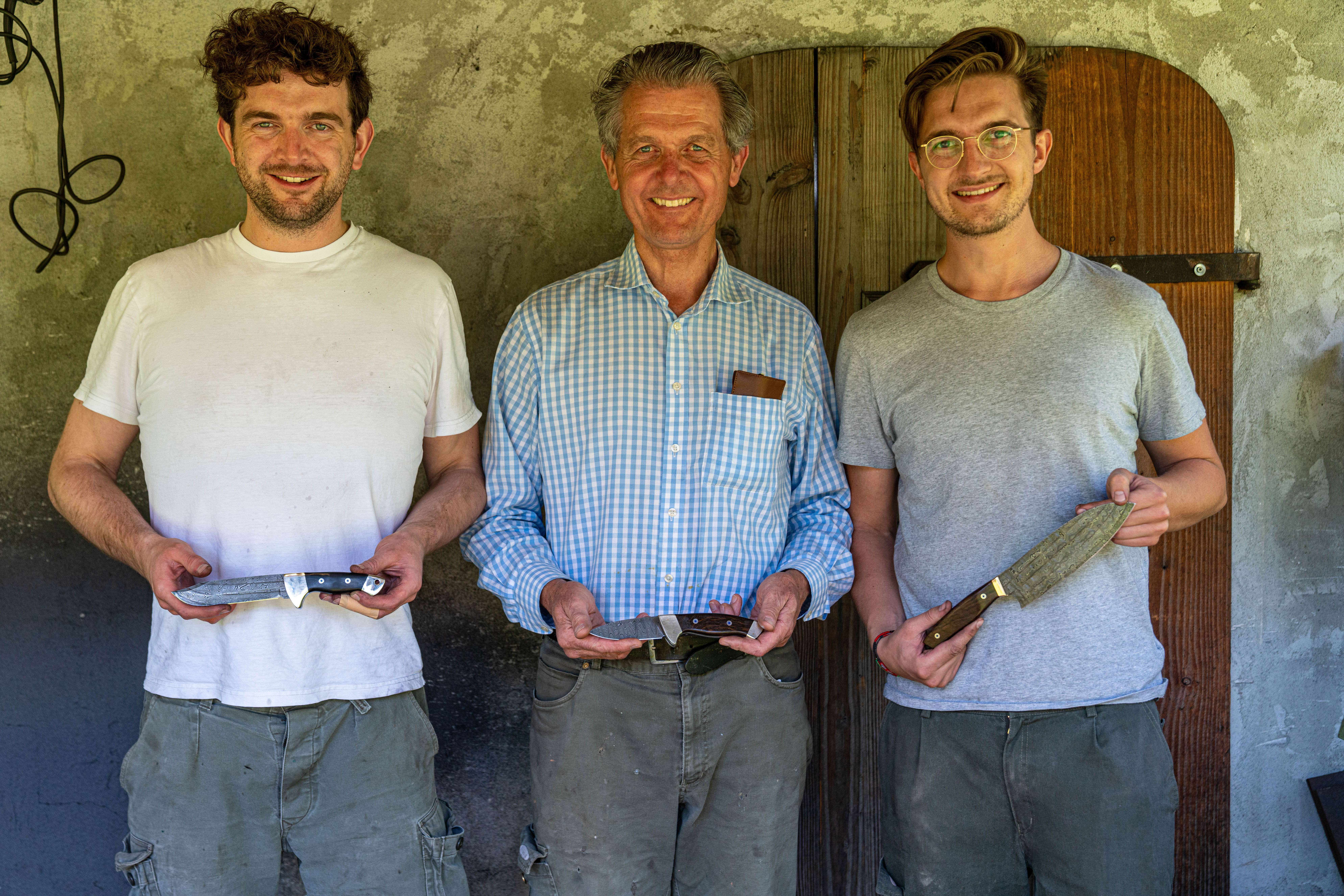 Drei strahlende Teilnehmer pr&auml;sentieren stolz ihre selbst geschmiedeten Messer &mdash; das Ergebnis des Flow