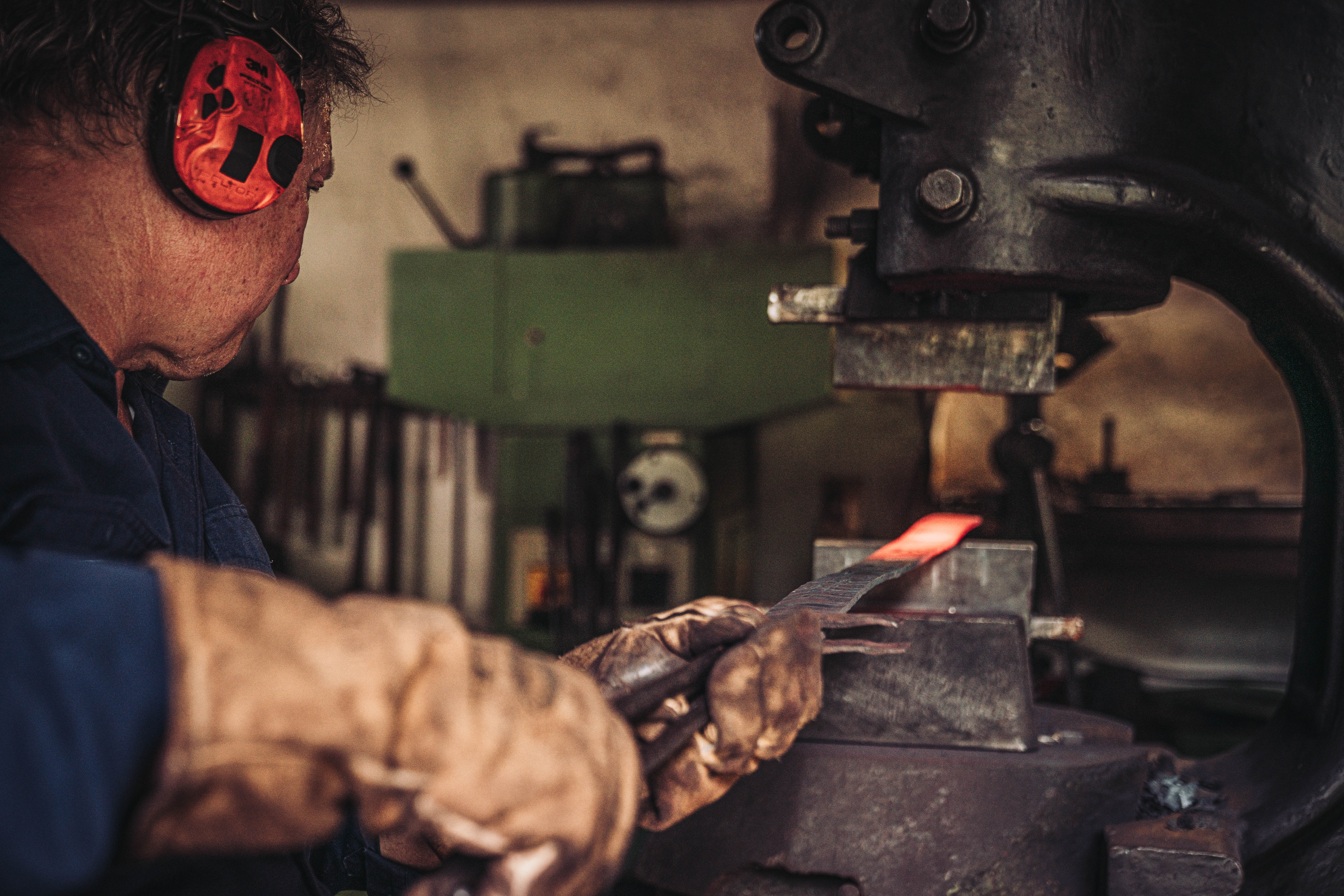 Wolf am Federhammer Ajax&nbsp;II &mdash; konzentrierter Blick auf den gl&uuml;henden Stahl, Lederhandschuhe und Geh&ouml;rschutz