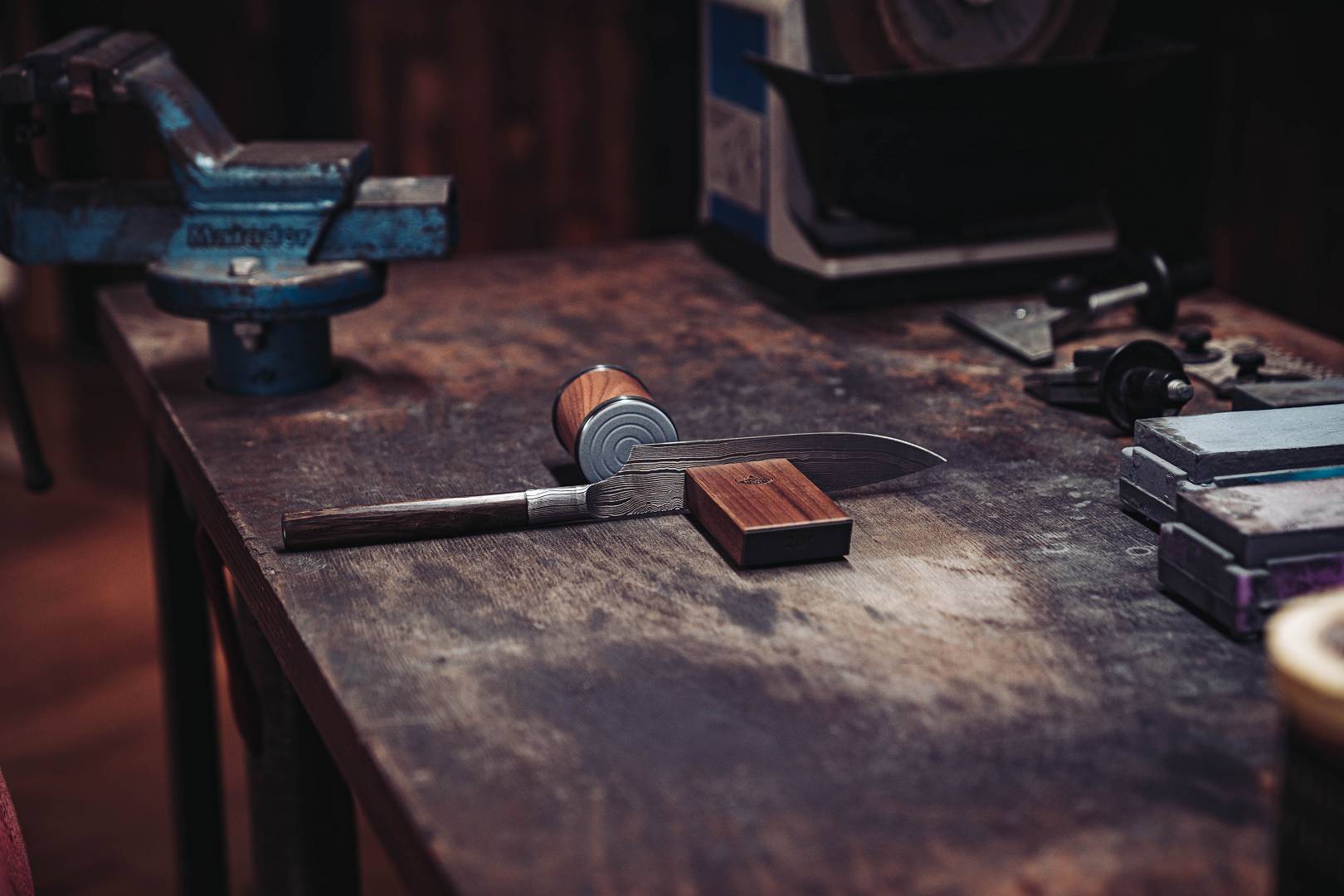 Damastmesser auf patinierter Werkbank mit Schraubstock und Schleifstein &mdash; Tradition trifft Gegenwart