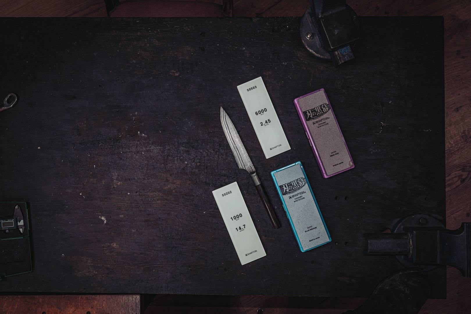 Vier Shapton Keramik-Schleifsteine verschiedener K&ouml;rnungen neben einer Damastklinge auf der Werkbank