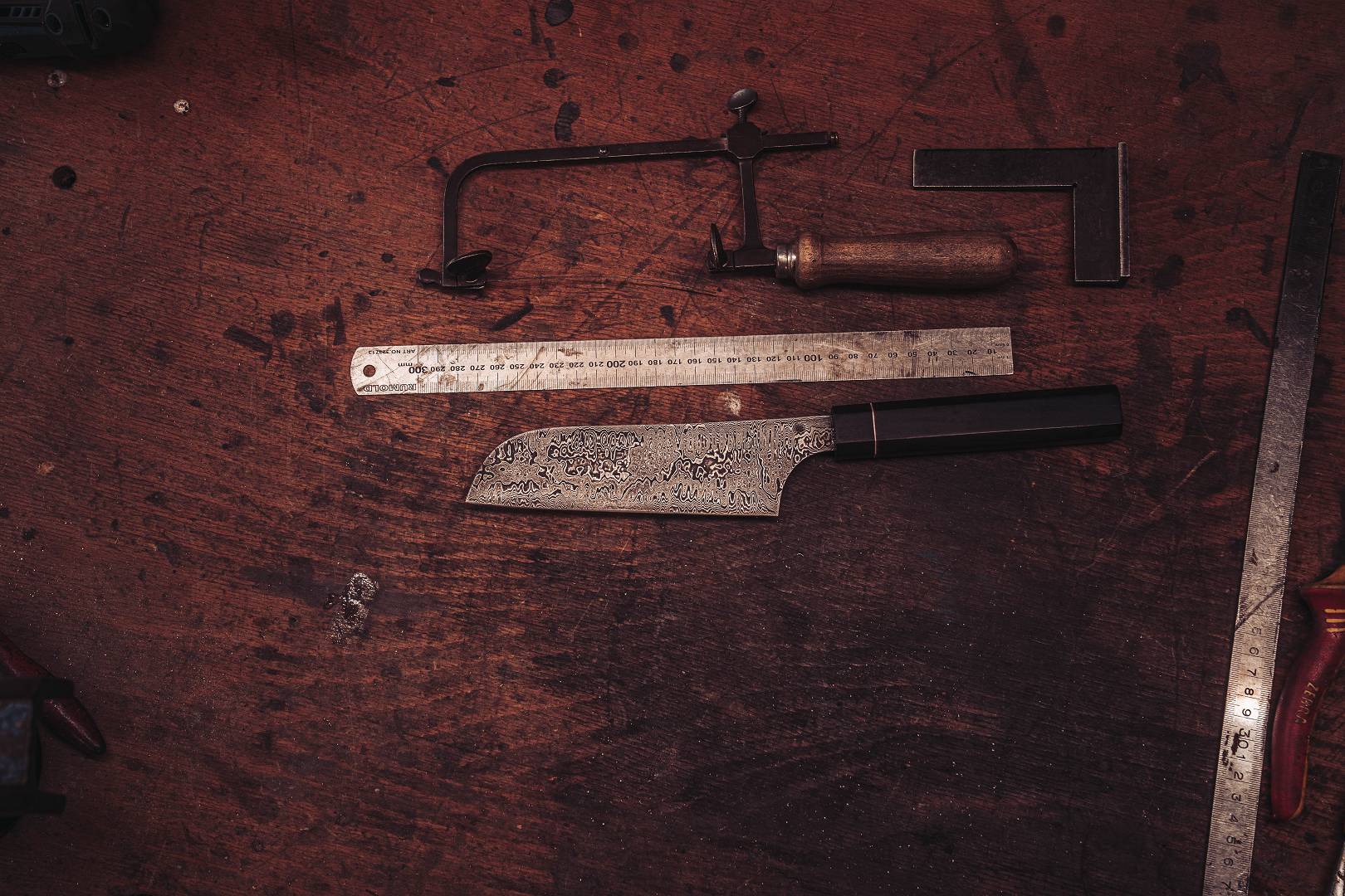 Damast-Nakiri auf Werkbank mit Laubsaege, Lineal und Winkel &mdash; japanische Kochmesser-Geometrie von oben