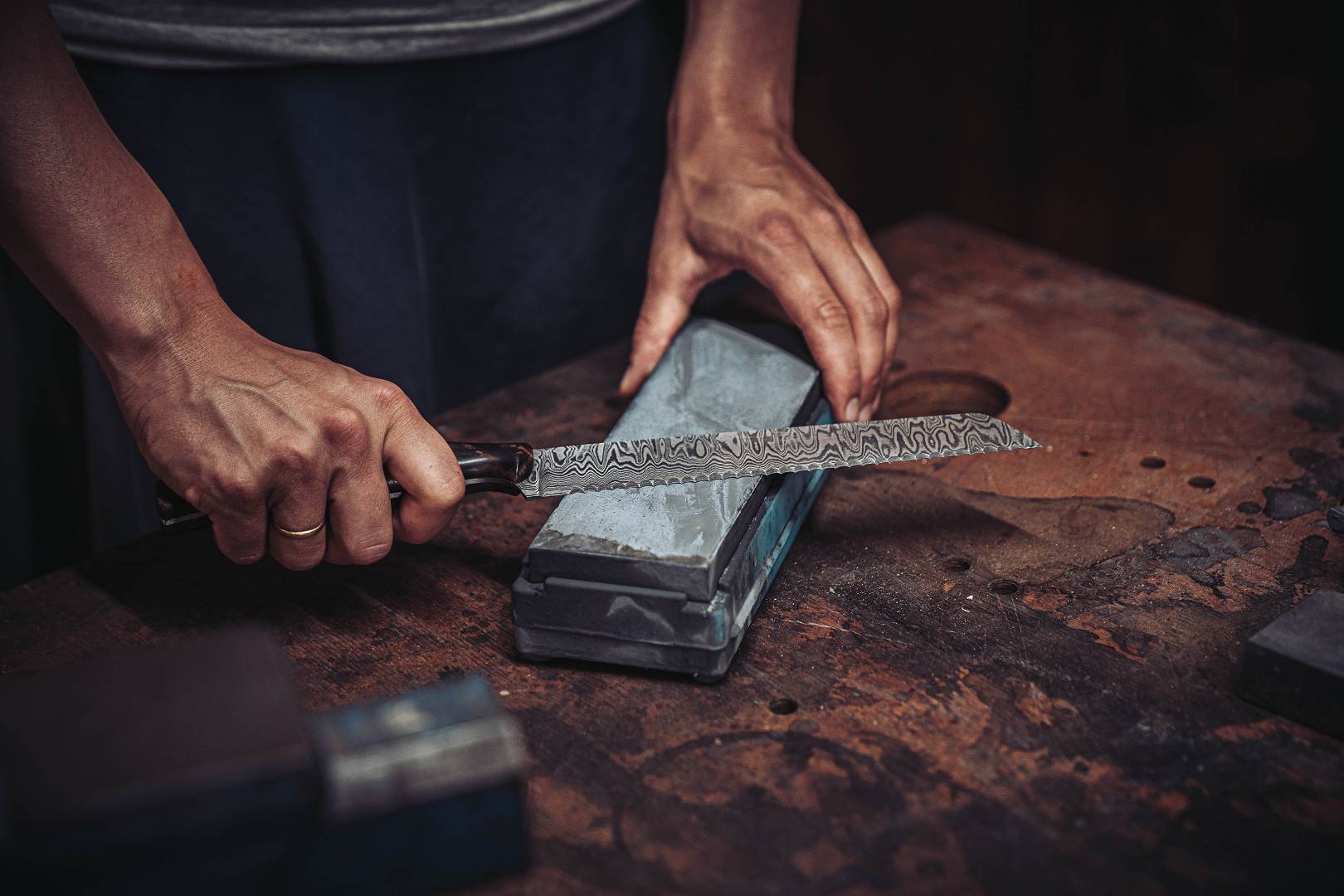 H&auml;nde sch&auml;rfen ein Damastmesser auf einem Wasserstein &mdash; kontrollierte Sch&auml;rfbewegung