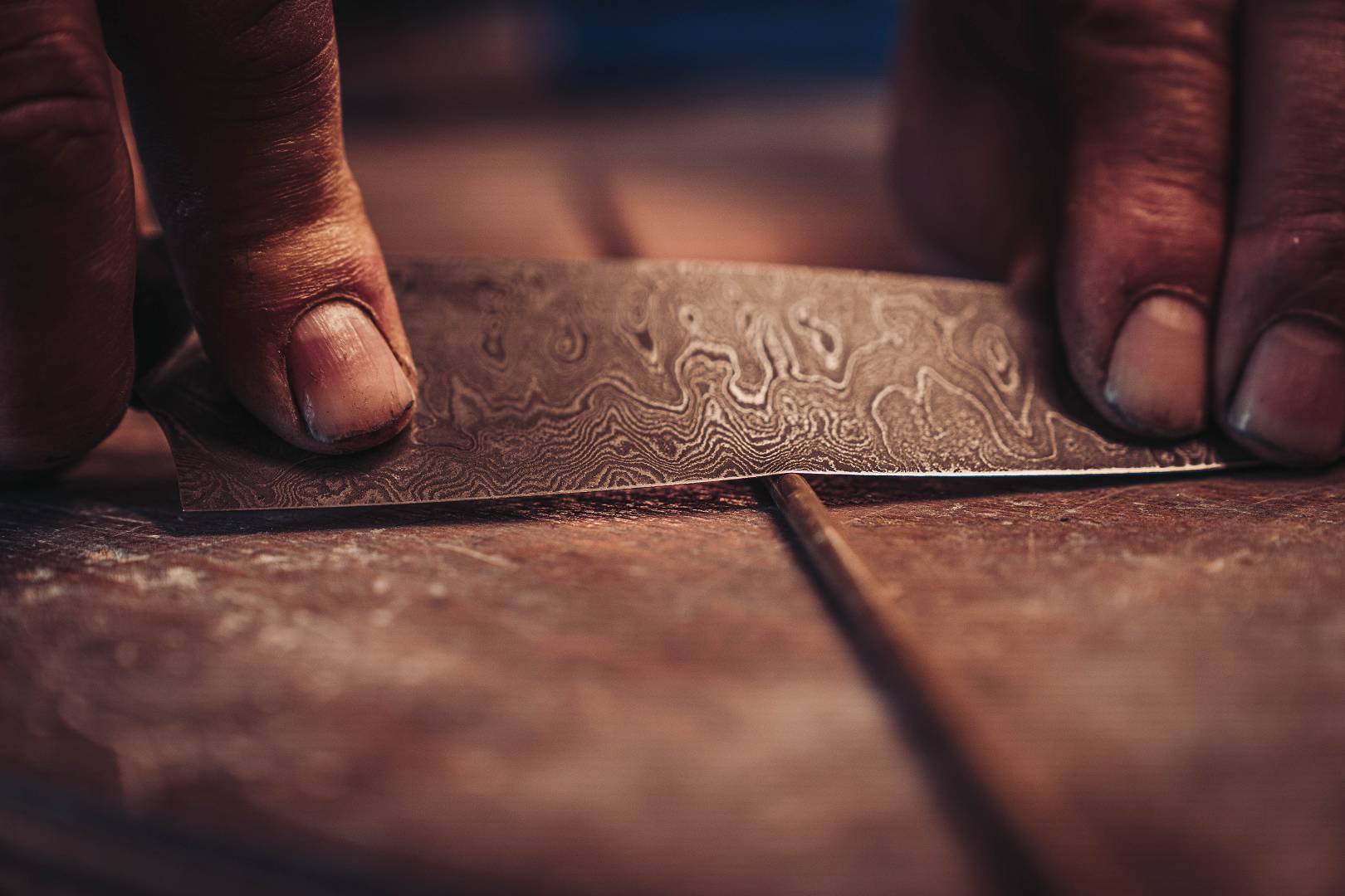 Damastmuster Nahaufnahme &mdash; Finger halten polierte Damastklinge mit sichtbarem Lagenmuster