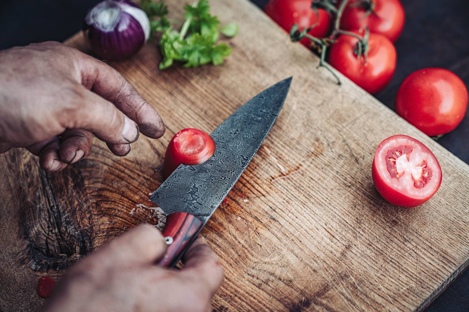 Damastmesser schneidet eine Tomate auf einem Holzbrett
